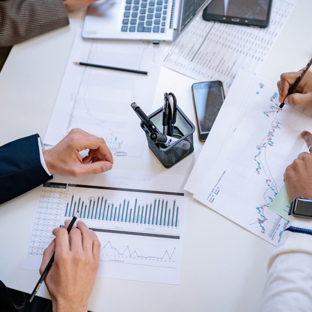 HR Metrics Consultants analysieren gemeinsam an einem Schreibtisch mit Laptops und Stiften verschiedene HR Kennzahlen und Diagramme im Rahmen der Digitalisierung von HR Prozessen.