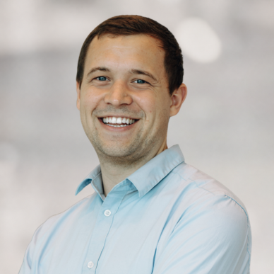 Lächelnder Mann in einem hellblauen Hemd vor einem unscharfen Hintergrund, der als Porträtfoto für die HR Metrics Consulting GmbH dient.